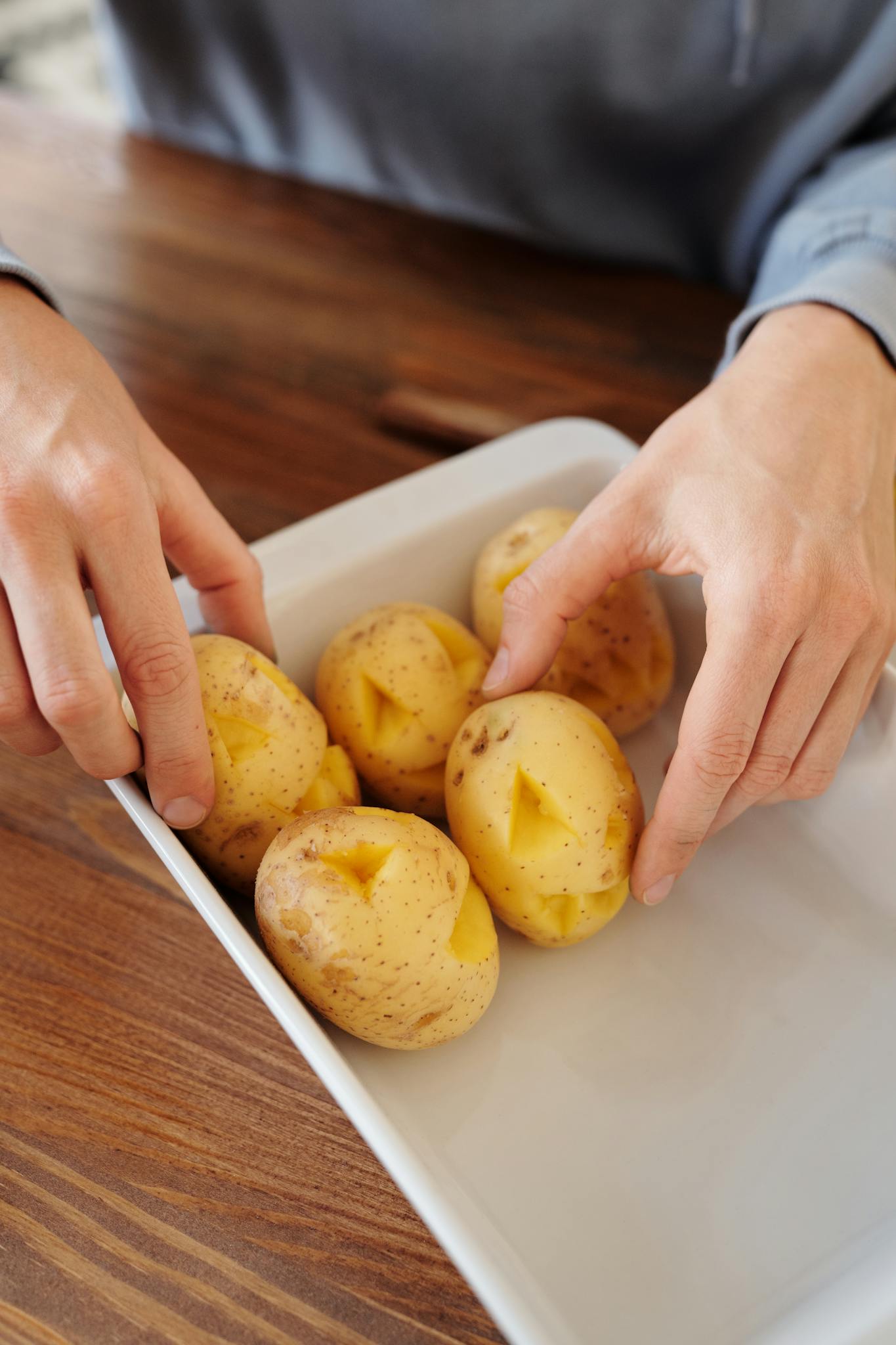 Hands arranging raw potatoes in a dish, ideal for cooking tutorials or organic food themes.